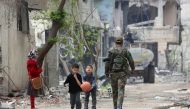 Syrian boys play with a basketball as a government soldier walks by down a street in the town of Hazzeh in Eastern Ghouta, on the outskirts of the Syrian capital Damascus, on March 28, 2018. / AFP / STRINGER