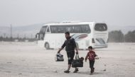 Members of a Syrian family evacuated from the town of Dumayr, east of the capital Damascus, carry their belongings as they walk away after disembarking from their bus in the city of Azaz in the northern countryside of Aleppo on April 20, 2018. AFP / Samee