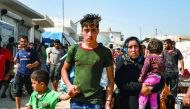 Men, women, and children walk past make-shift brick shelters at a camp for the displaced during a demonstration by Syrians along the border with Turkey near the town of Atme in the northwestern Idlib province on August 30, 2019 demanding Ankara help stop 