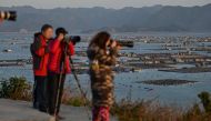 In this photo taken on December 12, 2019, Chinese tourists take photos as villages (back) on the sea are seen from Dong An Island in Xiapu in China's Fujian province. AFP / Hector Retamal 