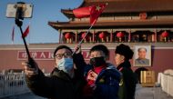  A boy waves a national flag as his dad holds him and uses a smartphone with a selfie stick to take a photo, both wearing protective masks, in front of the portrait of late communist leader Mao Zedong (R, back) at Tiananmen Gate in Beijing on January 23, 