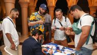 Tourists stand near an artist who is doing an Arabic calligraphy.