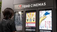 A cinema employee checks on a display showing a digital poster (R) for Oscar-winning animator Hayao Miyazaki's latest film, titled in English 