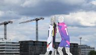 A worker climbs the 'Molecule Man' sculpture, designed by US artist Jonathan Borofsky wearing the three different Germany's national kits in the water of the river Spree in Berlin on June 13, 2024, ahead of the UEFA Euro 2024 European Football Championship. (Photo by Ralf Hirschberger / AFP)