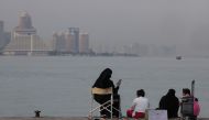 A family sits on the pavement along Doha Corniche on August 6, 2024. (Photo by Karim Jaafar / AFP)

