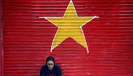 A street vendor uses her mobile phone as she sits in front of a garage door in the colours and shapes of the Vietnamese flag in Hanoi on August 28, 2024. (Photo by Nhac NGUYEN / AFP)
