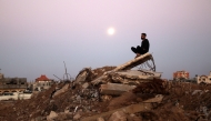 The full moon rises as a man sits atop a pile of rubble it the al-Bureij refugee camp in the central Gaza Strip on November 15, 2024, amid the ongoing war between Israel and the Hamas militant group. (Photo by Eyad BABA / AFP)