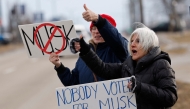 People hold signs during a protest against Elon Musk outside of a Tesla dealership in West Bloomfield, Michigan, on February 27, 2025. (Photo by Jeff Kowalsky / AFP)