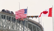 The US and Canadian flags fly on the US side of the St. Clair River near the Bluewater Bridge border crossing on January 29, 2025. (Photo by Geoff Robins / AFP)