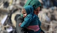 A Palestinian woman carries a baby as families leave the eastern sector of the Gaza Strip on the border with Israel following Israeli airstrikes that targeted northern and other parts of Gaza in the early hours of March 18, 2025. Gaza's civil defence agency said the death toll from a massive Israeli campaign launched throughout the Palestinian territory rose to more than 400 people, including children. Photo by Bashar TALEB / AFP.