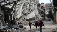 People walk past a building destroyed during Israeli strikes at the Nusseirat refugee camp, on March 20, 2025. Photo by Eyad BABA / AFP