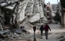 People walk past a building destroyed during Israeli strikes at the Nusseirat refugee camp, on March 20, 2025. Photo by Eyad BABA / AFP