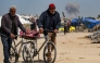 Two elderly men walk pushing bicycles while behind a cloud of smoke erupts from Israeli bombardment on the northern Gaza Strip, in Beit Lahia on March 25, 2025. Photo by Bashar TALEB / AFP