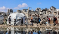  People walk past a puddle of water by a tent shelter erected near the rubble of a collapsed building in the Nasr neighbourhood in western Gaza City on April 15, 2025. Photo by Omar AL-QATTAA / AFP