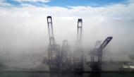 This aerial view shows container cranes amid the clouds at the Port of Ensenada in Baja California state, Mexico on April 11, 2025. (Photo by Guillermo Arias / AFP)
