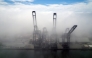 This aerial view shows container cranes amid the clouds at the Port of Ensenada in Baja California state, Mexico on April 11, 2025. (Photo by Guillermo Arias / AFP)
