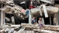 A boy and girl sit by the ruins of a destroyed building in Gaza City on April 21, 2025. (Photo by Omar Al Qattaa / AFP)