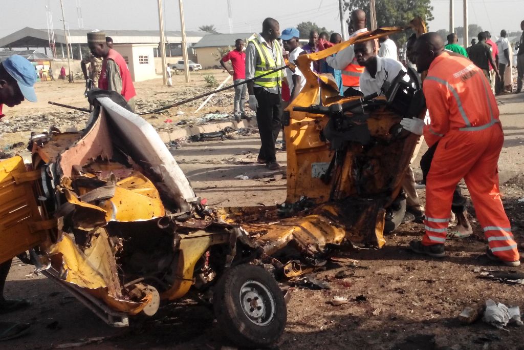 Emergency personnel stand near the wreacked remains of a vehicle ripped apart following two suicide bombings in Nigeria's northeast city of Maiduguri on October 29, 2016 where at least nine people and scores of others were injured. / AFP / JOSHOUA OMIRIN