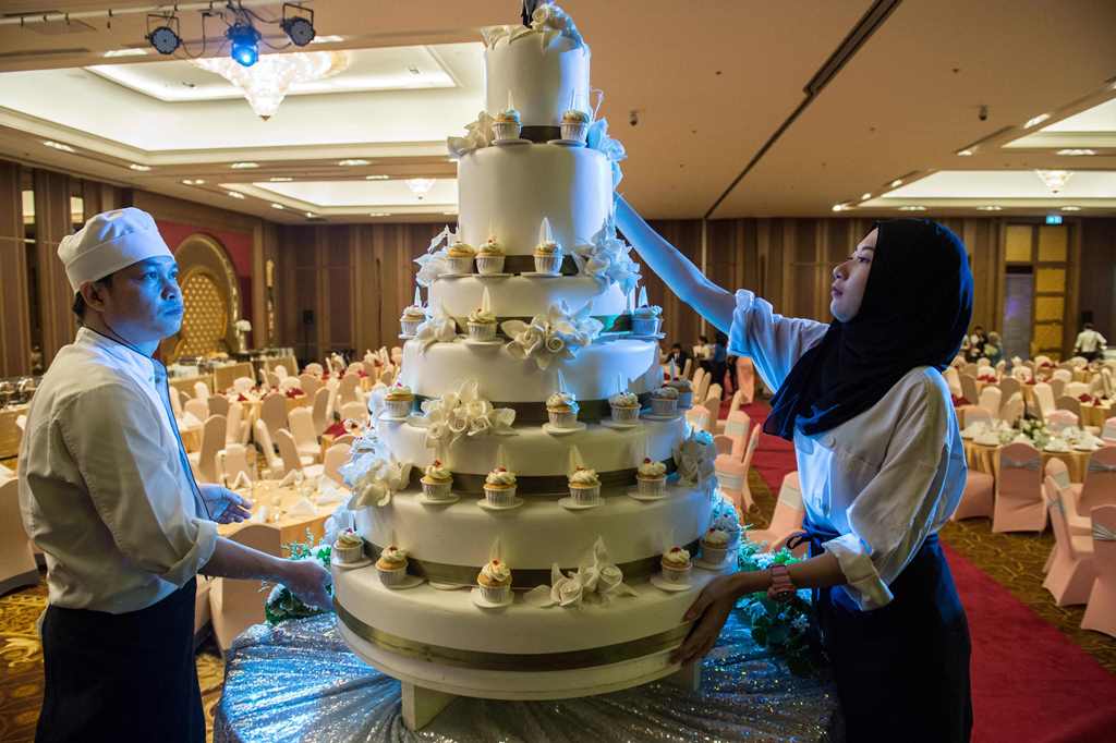 In this photograph taken on January 15, 2017, pastry chefs adorn a wedding cake before a wedding reception at the Al Meroz hotel in Bangkok. AFP / Roberto Schmidt 
