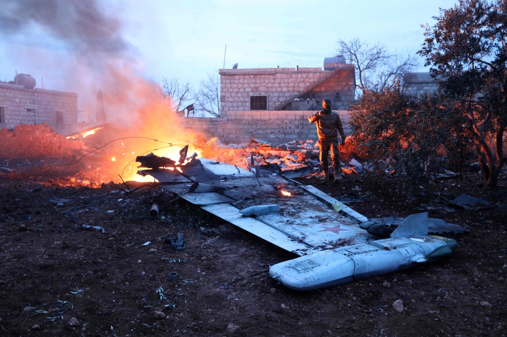 A picture taken on February 3, 2018, shows a Rebel fighter taking a picture of a downed Sukhoi-25 fighter jet in Syria's northwest province of Idlib.   AFP / OMAR HAJ KADOUR