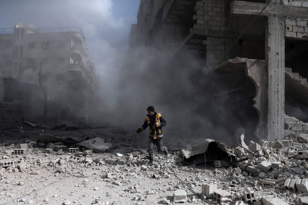 A civil Defence volunteer, known as the White Helmets, checks the site of a regime air strike in the rebel-held town of Saqba, in the besieged Eastern Ghouta region on the outskirts of the capital Damascus, on February 23, 2018.  AFP / ABDULMONAM EASSA
