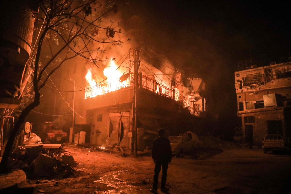 TOPSHOT - A picture taken early on March 23, 2018 shows a man standing looking at flames erupting in a building following regime bombardment in Douma, one of the few remaining rebel-held pockets in Eastern Ghouta on the outskirts of the capital Damascus. 