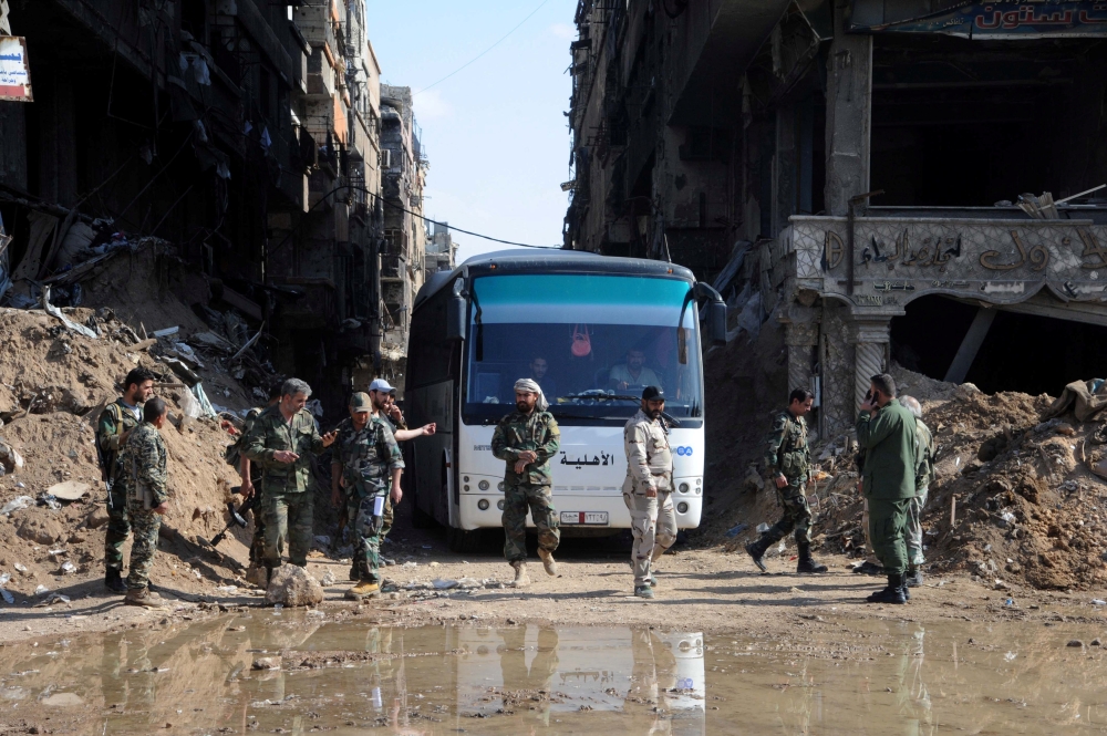 Soldiers loyal to Syria's President Bashar al Assad are seen near a bus carrying rebels from Yarmouk Palestinian camp in Damascus, Syria April 30, 2018. Picture Taken April 30, 2018. SANA
