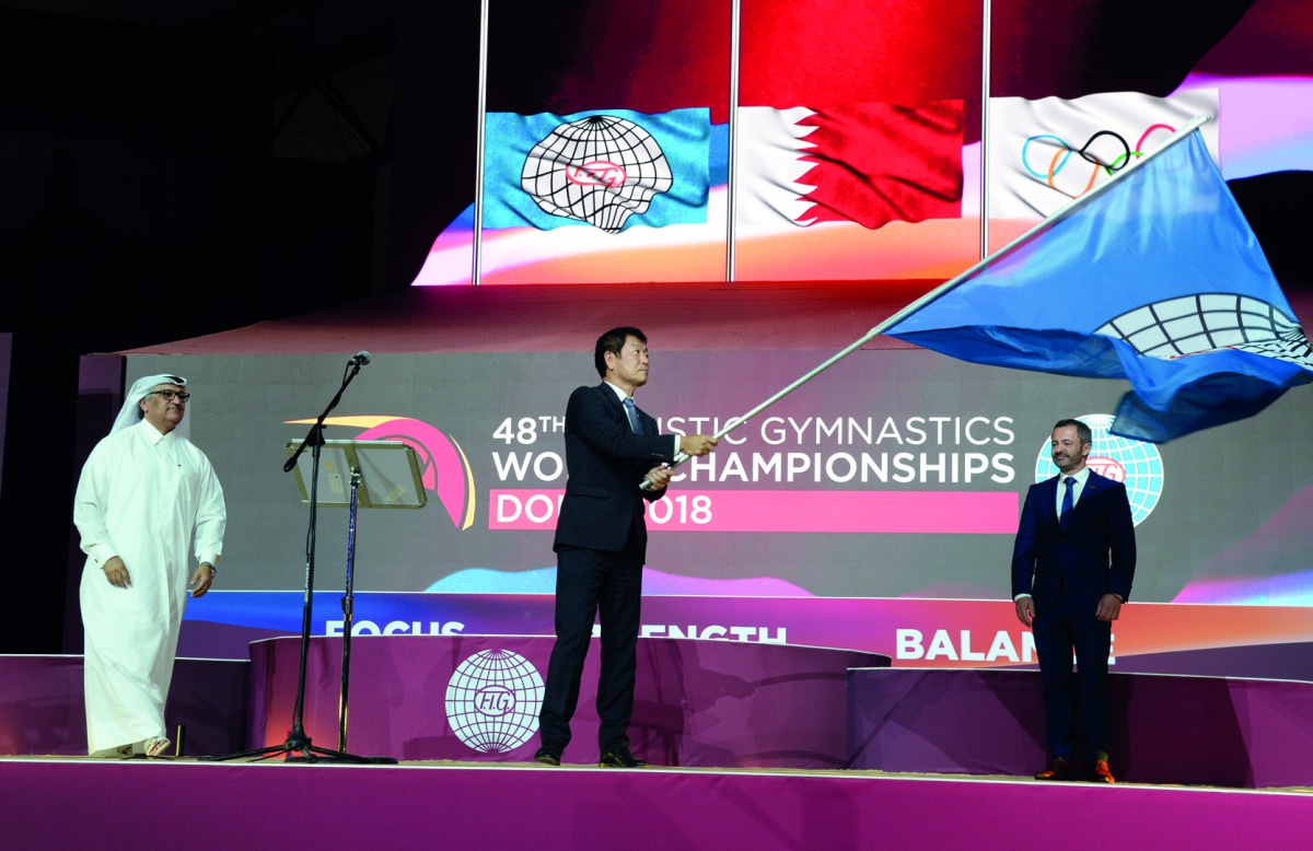 FIG President Morinari Watanabe (centre) waves the FIG flag after receiving the same from Ali Al Hitmi (left), the Executive Director of the Organising Committee of Doha Worlds and also President of the Qatar Gymnastics Federation during the closing cerem