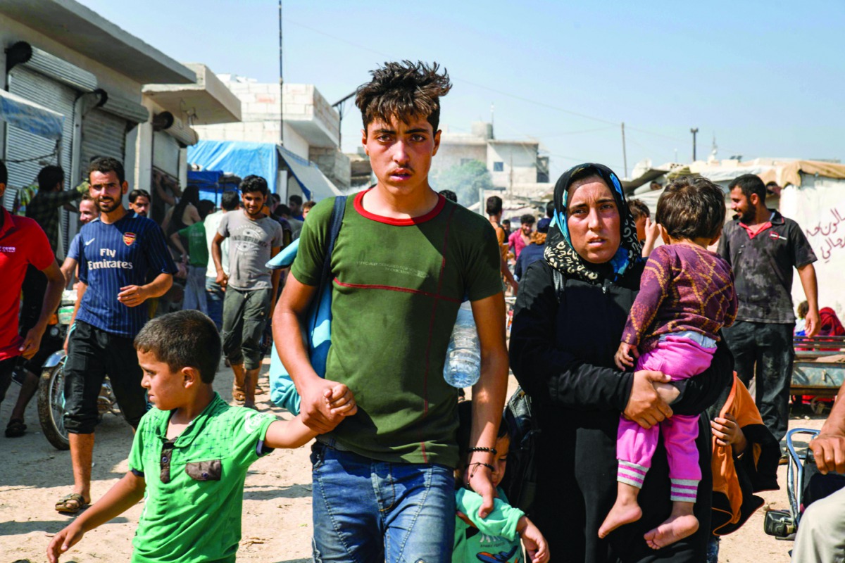 Men, women, and children walk past make-shift brick shelters at a camp for the displaced during a demonstration by Syrians along the border with Turkey near the town of Atme in the northwestern Idlib province on August 30, 2019 demanding Ankara help stop 