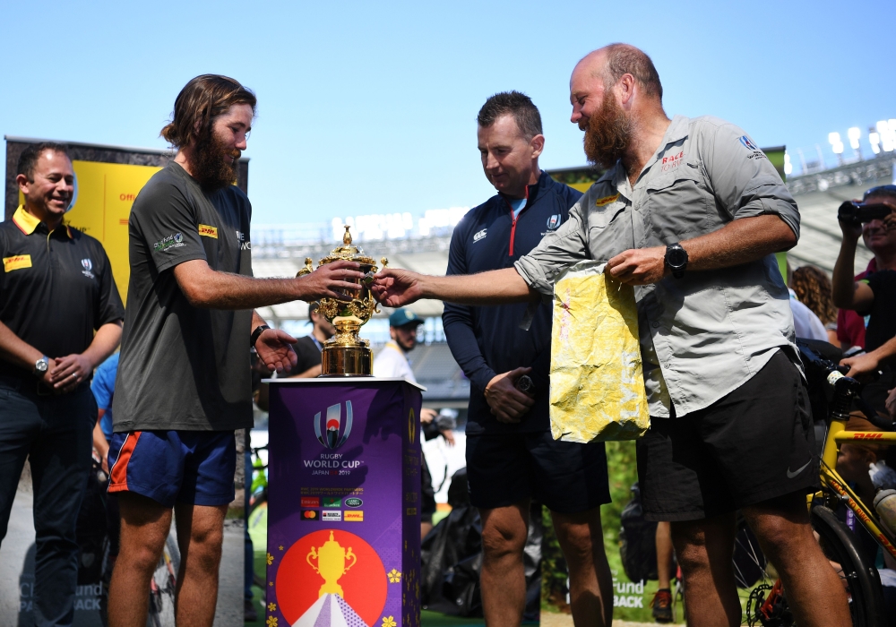 Ron Rutland (R) and James Owen (2nd L) deliver the whistle to be used in the opening Japan 2019 Rugby World Cup match to referee Nigel Owens (2nd R) at the Tokyo stadium in Tokyo on September 19, 2019, as they complete their bike expedition from Twickenha