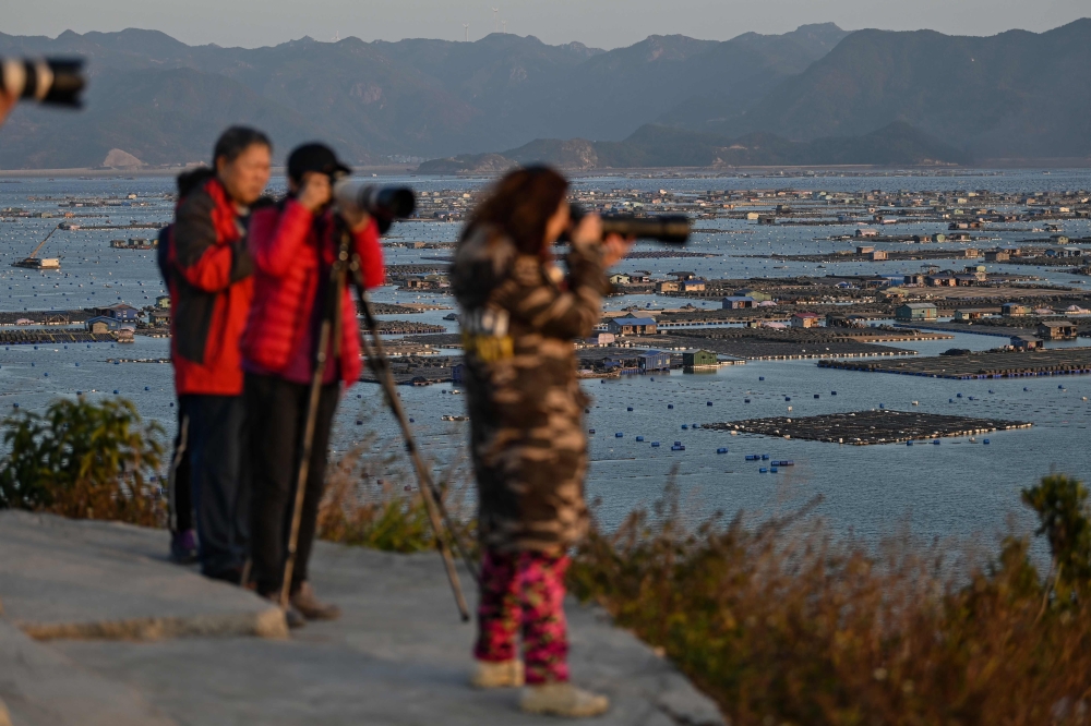 In this photo taken on December 12, 2019, Chinese tourists take photos as villages (back) on the sea are seen from Dong An Island in Xiapu in China's Fujian province. AFP / Hector Retamal 