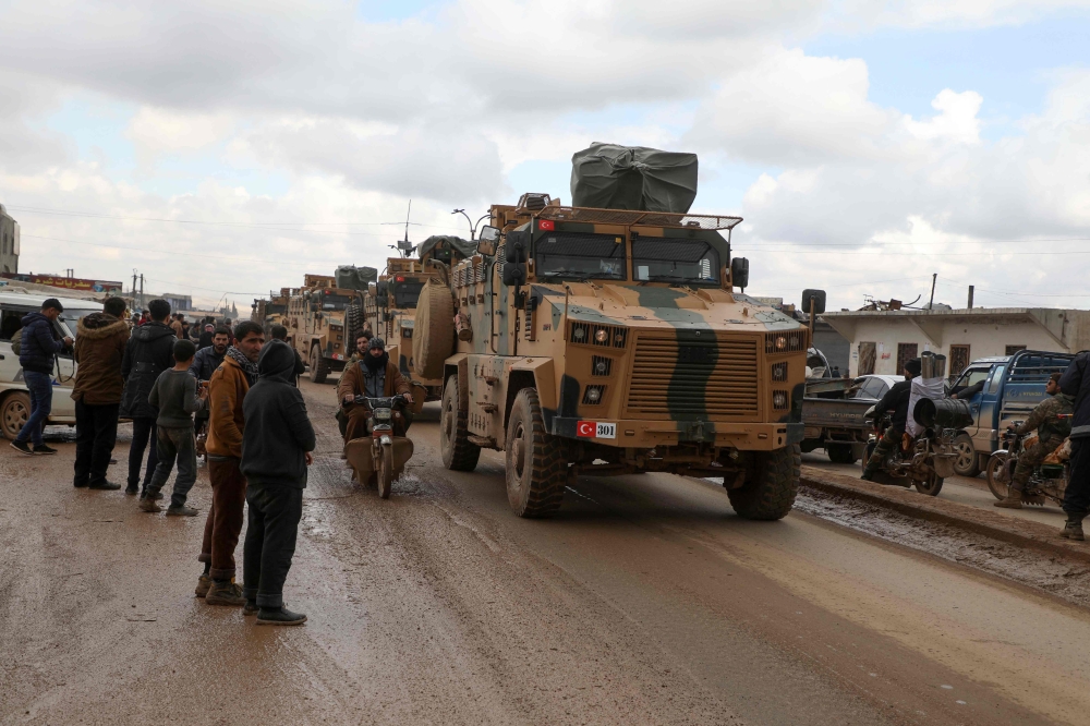 Residents watch as a Turkish military convoy that crossed from the border with Syria passes through the Syrian rebel-held town of Hazano in Idlib's northern countryside, on February 22, 2020. / AFP / AAREF WATAD