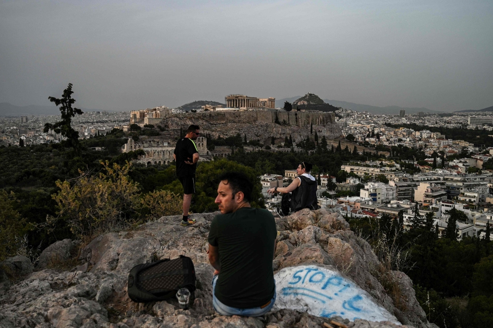 (FILES) In this file photo taken on May 17, 2020 people sit on a hill facing the ancient Temple of Parthenon atop the Acropolis hill in Athens on May 17, 2020 during the gradual deconfinement started on May 4, following a lockdown aimed at curbing the spr