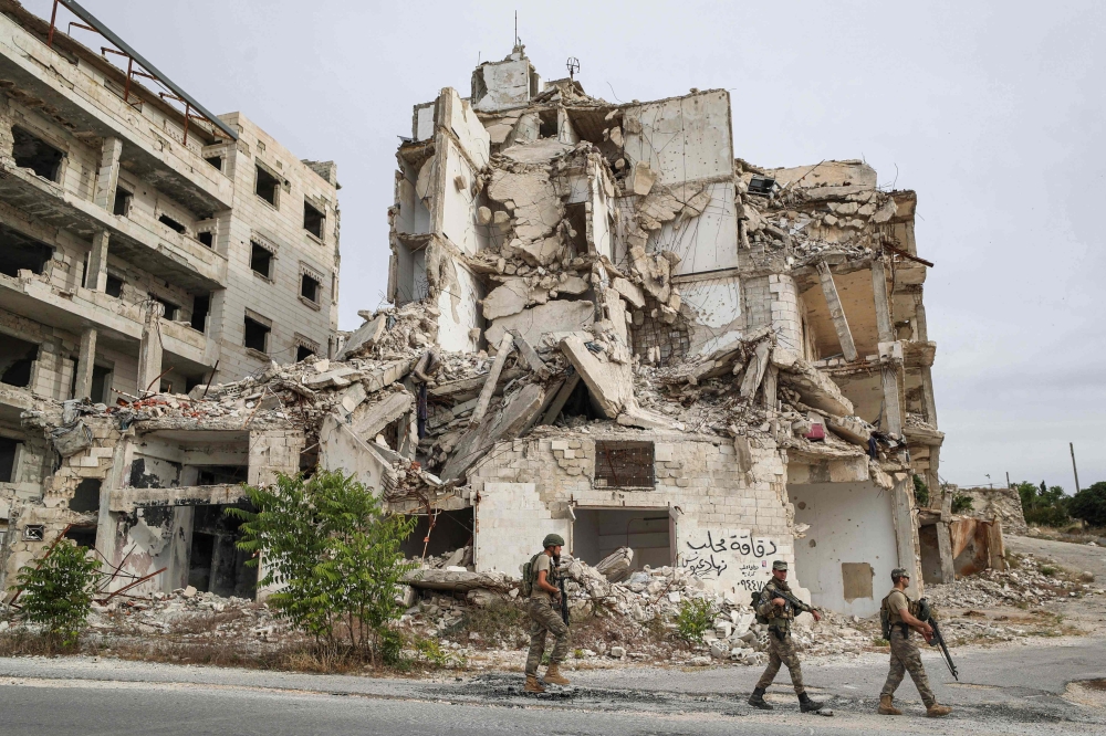 Turkish soldiers patrol along a road past destroyed buildings atop the Arbaeen hill overlooking Ariha in the southern countryside of Syria's Idlib province on May 26, 2020. / AFP / OMAR HAJ KADOUR