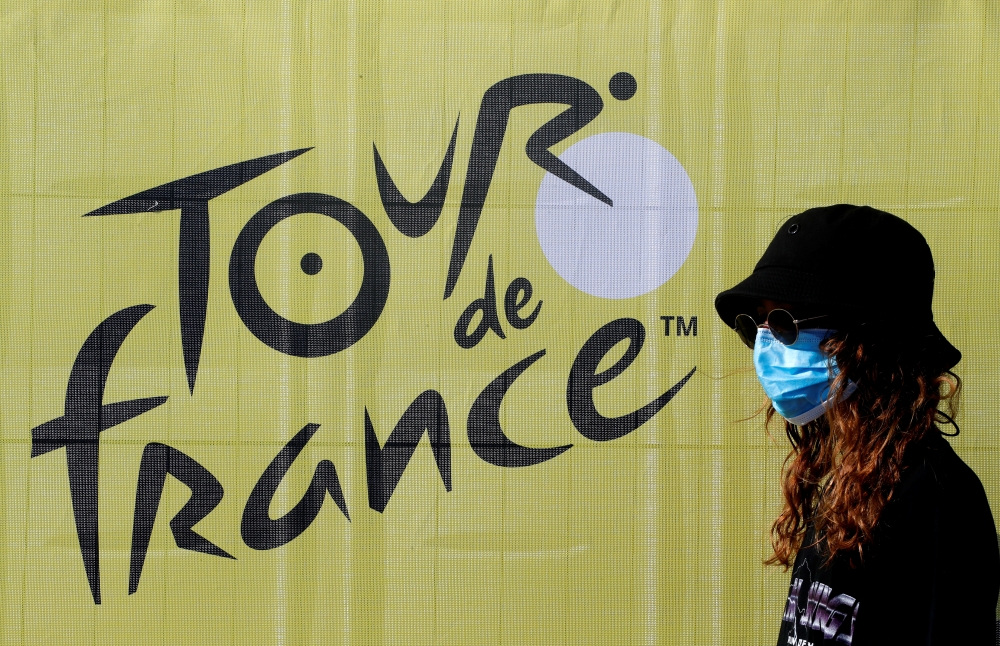 August 26, 2020 A person wearing a protective face mask walks past a sign ahead of the Tour de France REUTERS/Eric Gaillard