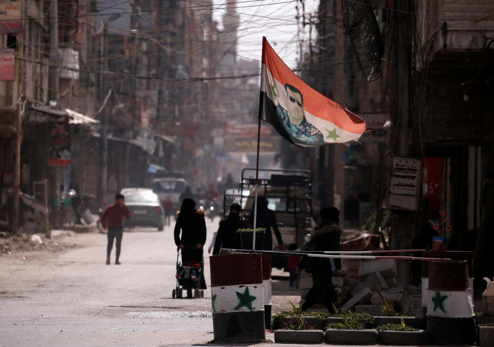 A national flag depicting a picture of Syria's President Bashar al-Assad flutters at a checkpoint in Douma, in the eastern suburbs of Damascus, Syria March 10, 2021. Picture taken March 10, 2021. REUTERS/Omar Sanadiki