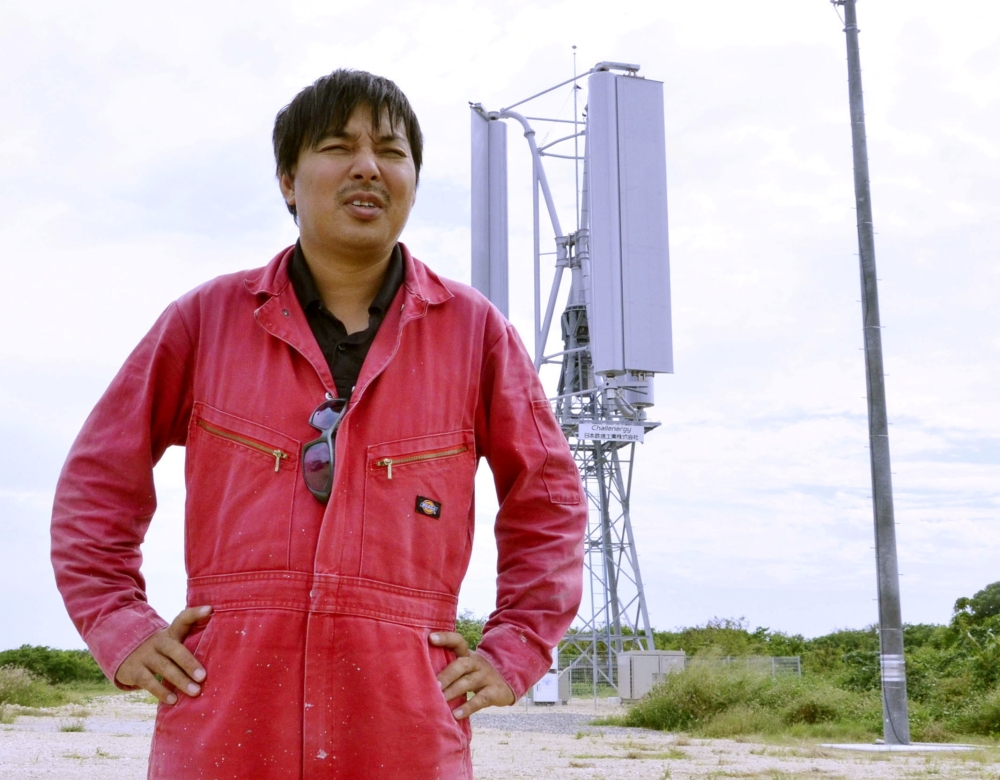 Challenergy's President and Chief Executive Atsushi Shimizu stand stands in front of the company's Magnus Vertical Axis Wind Turbine, which can work in cyclonic conditions, in Ishigaki on Japanese southern island of Ishigaki, Okinawa prefecture, November 