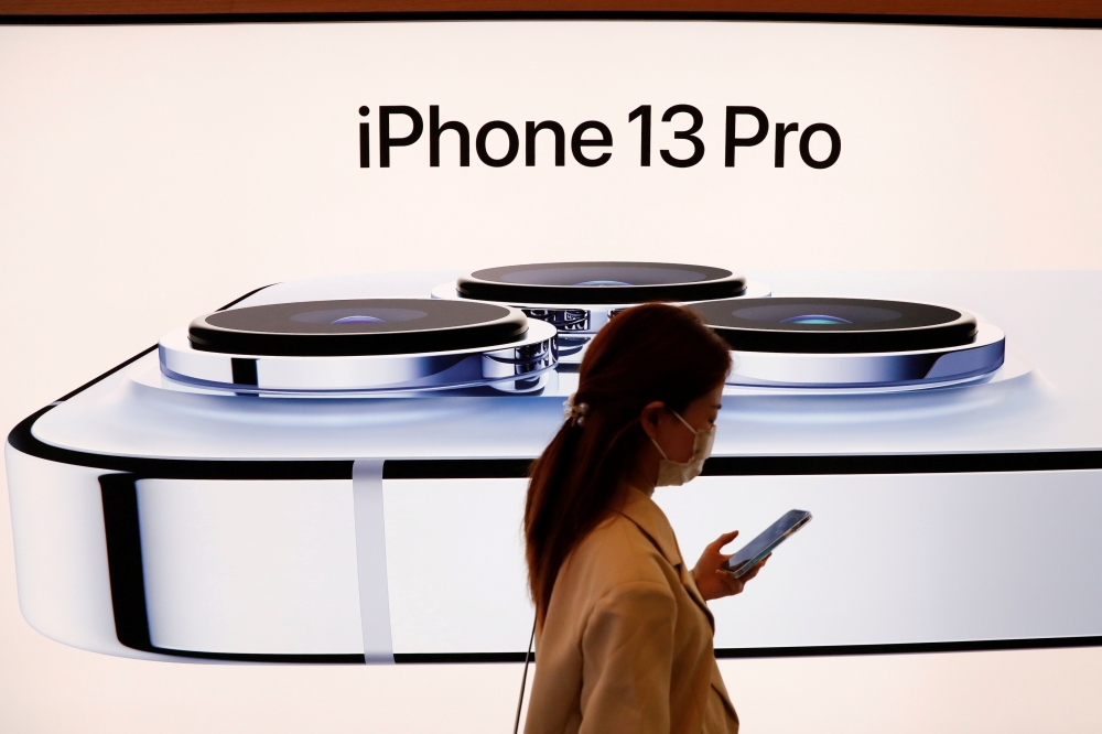 A woman wearing a face mask walks past an image of an iPhone 13 Pro at an Apple Store in Beijing, China, September 24, 2021. REUTERS/Carlos Garcia Rawlins/File Photo