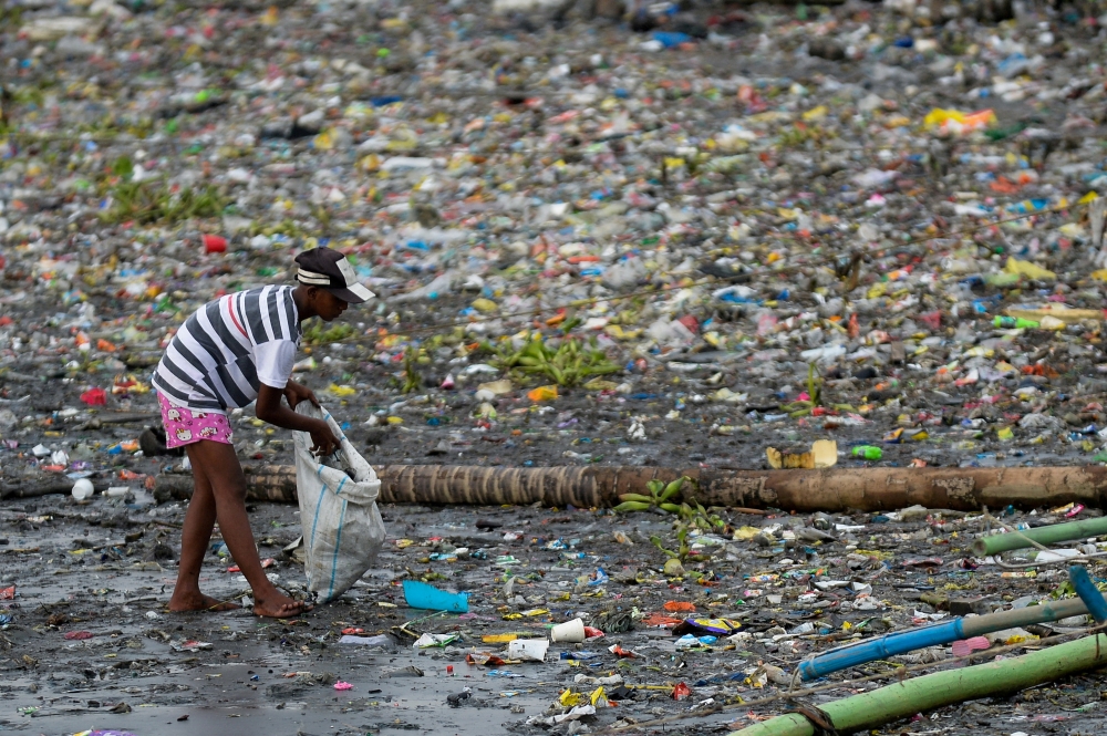 A woman picks up plastic cups along the riverbank of Pasig river, in Manila, Philippines, June 10, 2021. REUTERS/Lisa Marie David/File Photo