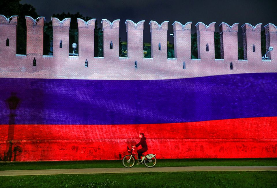 A woman rides a bicycle past a part of the Kremlin wall where the Russian national flag is projected, during celebrations of Russia Day in Moscow, Russia, June 12, 2020. REUTERS/Maxim Shemetov/File Photo

