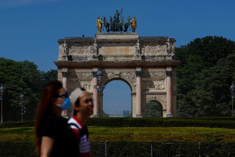 People walk past the Arc de Triomphe du Carrousel next to the Louvre museum on a sunny day in Paris, France, May 11, 2022. REUTERS/Gonzalo Fuentes