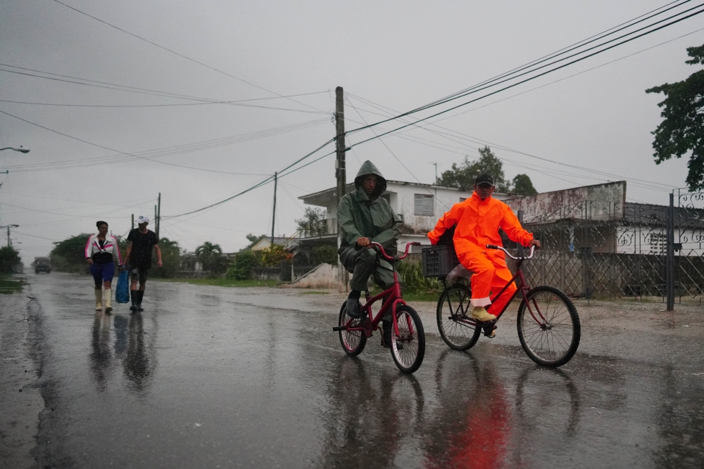 People walk under the rain ahead of the arrival of Hurricane Ian in Coloma, Cuba, September 26, 2022. REUTERS/Alexandre Meneghini