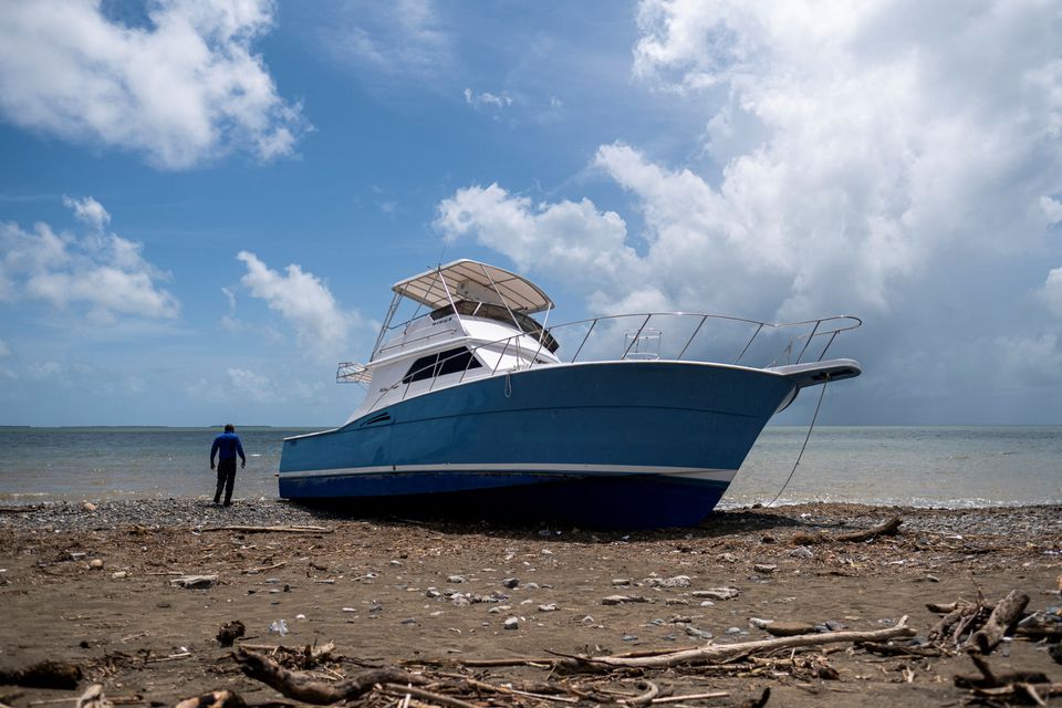 A man stands next to a washed up boat on the beach after Hurricane Fiona in Santa Isabel, Puerto Rico September 21, 2022. REUTERS/Ricardo Arduengo
