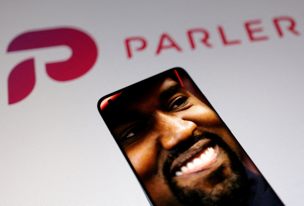 American rapper Kanye West's picture is seen on a smartphone in front of the logo of social media app Parler in this Illustration taken October 17, 2022. (REUTERS/Dado Ruvic)