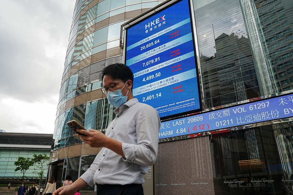 People walk past a screen displaying the Hang Seng stock index outside Hong Kong Exchanges, in Hong Kong, China July 19, 2022. Reuters/Lam Yik
