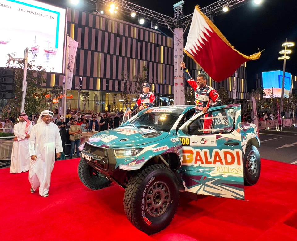 Nasser Saleh Al Attiyah waves Qatar's flag as QMMF President Abdulrahman Al Mannai walks on during the ceremonial start at Lusail Boulevard, yesterday.  