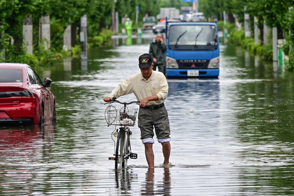 A man pushes a bicycle down a road closed due to flooding at Koshigaya, Saitama Prefecture on June 3, 2023. (Photo by JIJI Press / AFP) 