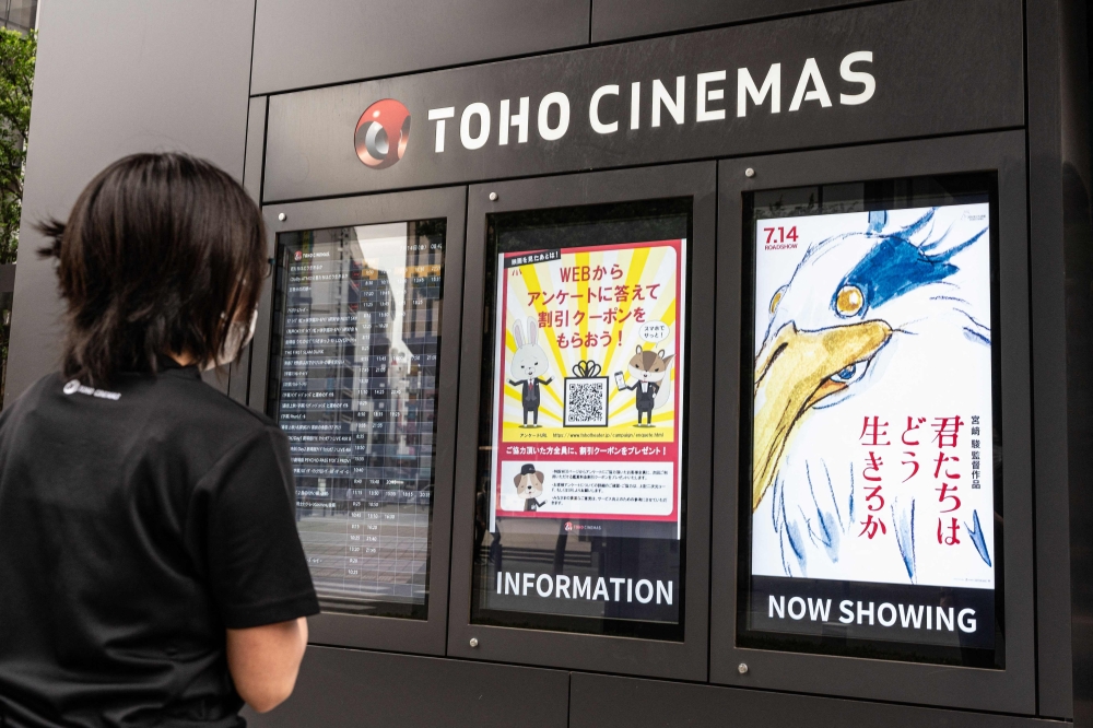 A cinema employee checks on a display showing a digital poster (R) for Oscar-winning animator Hayao Miyazaki's latest film, titled in English 