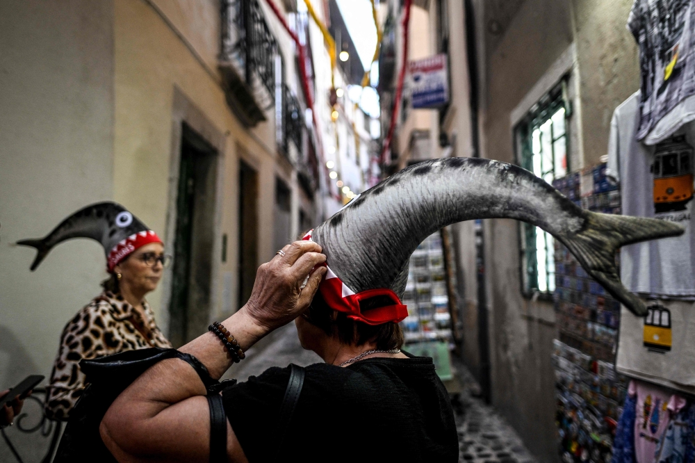 Women are pictured wearing a “sardine hat” at Alfama neighborhood in Lisbon, on June 12, 2023. (Photo by Patricia De Melo Moreira / AFP)