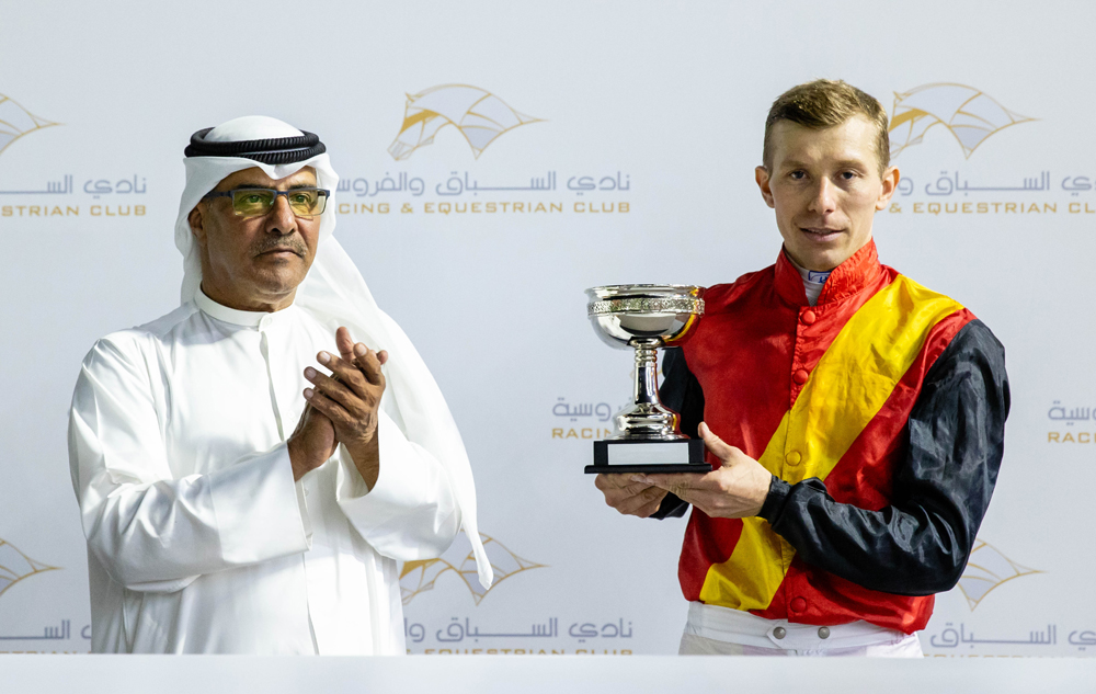 Jockey Szczepan Mazur poses after receiving his trophy from QREC Racing Manager Abdulla Rashid Al Kubaisi.